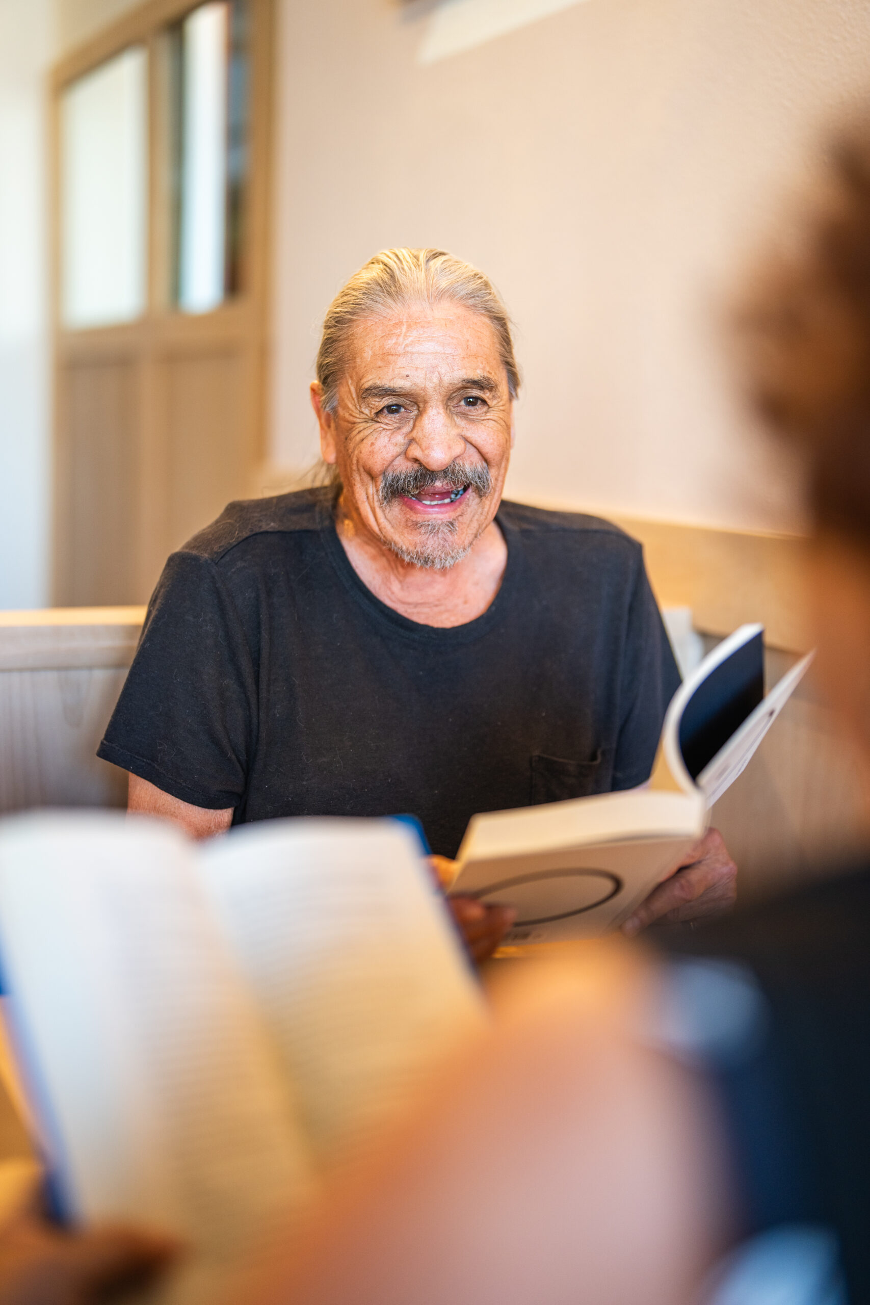 Older man in a café reading a book with his wife